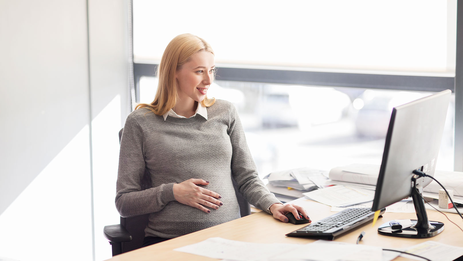Eine schwangere Geschäftsfrau sitzt in ihrem Büro am Computer.